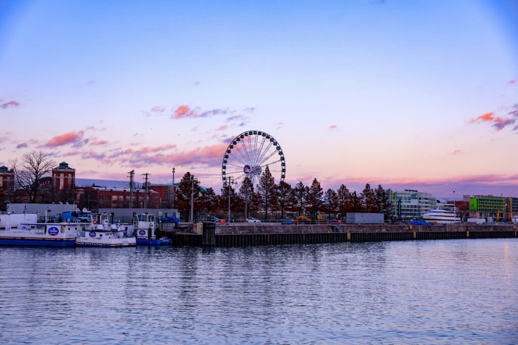 View of Chicago’s Navy Pier Ferris wheel at sunset with calm lake water, pastel pink clouds, and skyline buildings in the background.