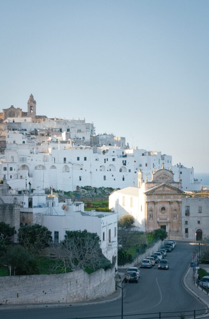 Alberobello trulli houses at dawn with no crowds and the conical roofs catching the early morning light, Ostuni old town glowing white under the afternoon sun with olive groves stretching to the horizon behind it