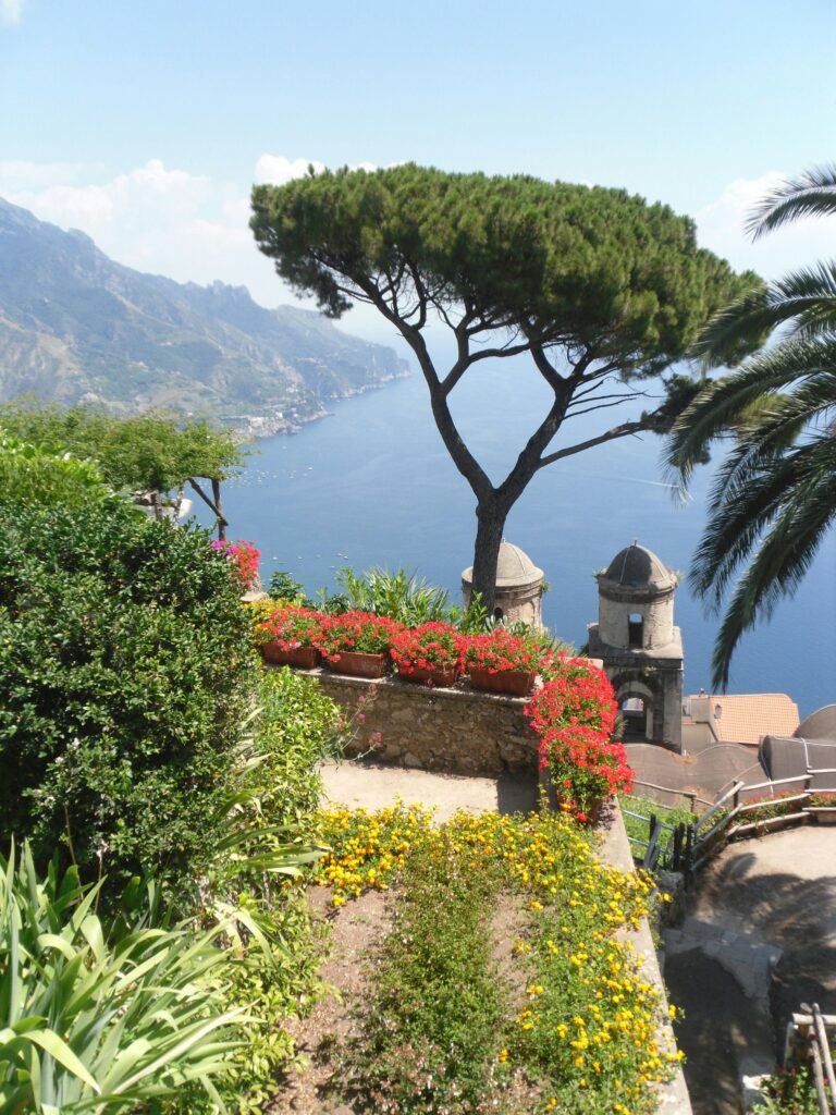 Scenic view from Villa Rufolo gardens in Ravello with flowers, pine trees, and the Amalfi Coast coastline below.