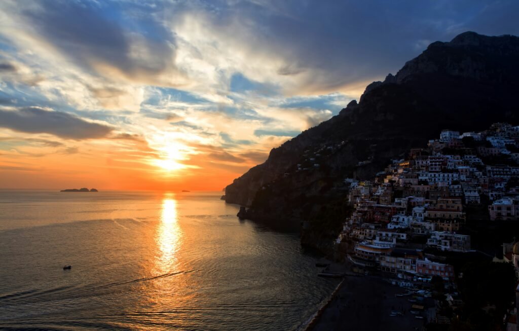 Positano waterfront at sunset with colorful cliffside buildings and the sea glowing golden