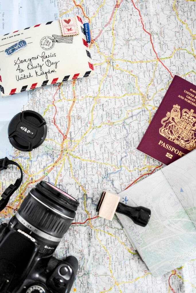 Travel planning flat lay with passport, road map, camera, airmail envelope and notebook on a table.