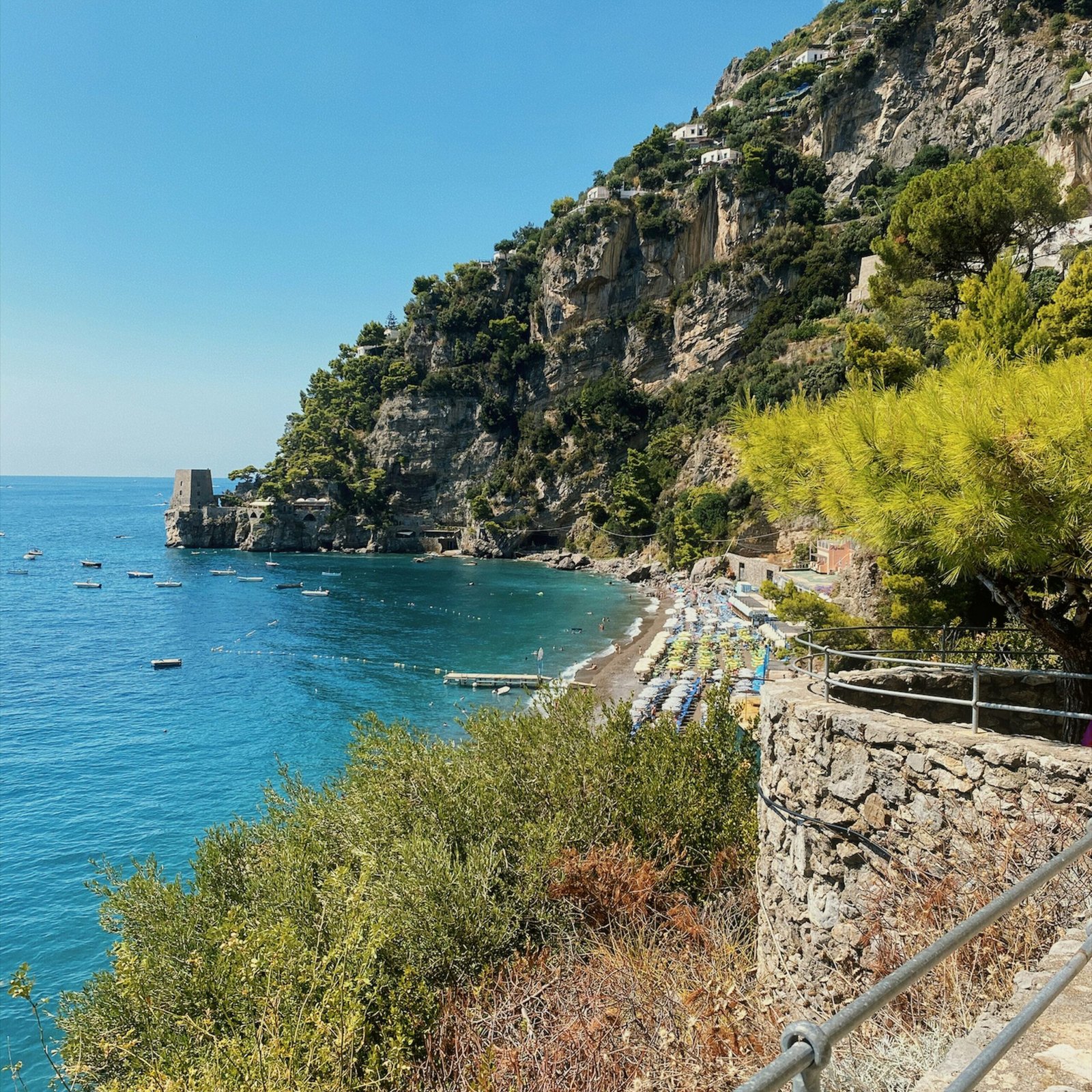 Scenic view of Positano beach with turquoise sea, sunbeds, and steep cliffs on Italy’s Amalfi Coast.