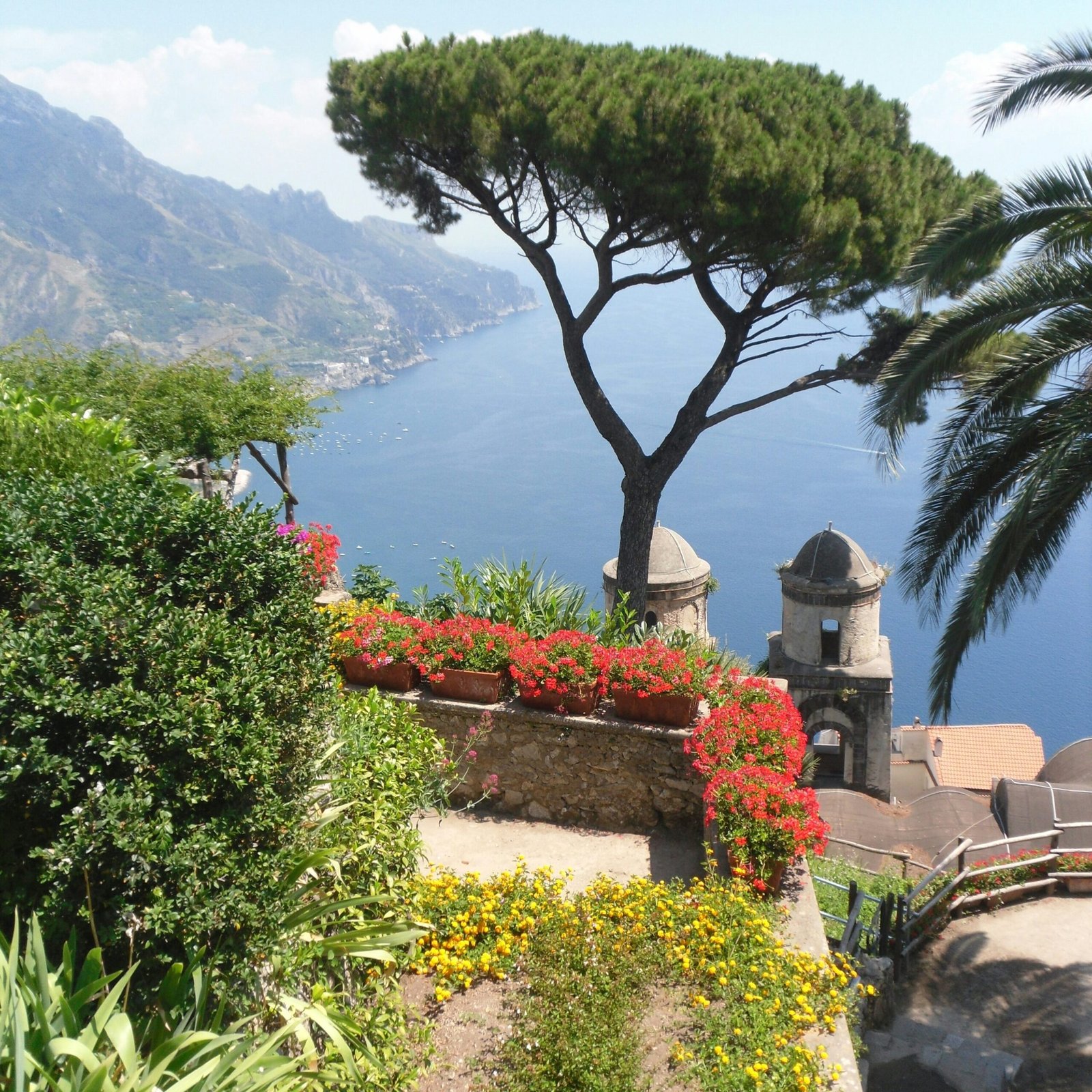 Scenic view from Villa Rufolo gardens in Ravello with flowers, pine trees, and the Amalfi Coast coastline below.