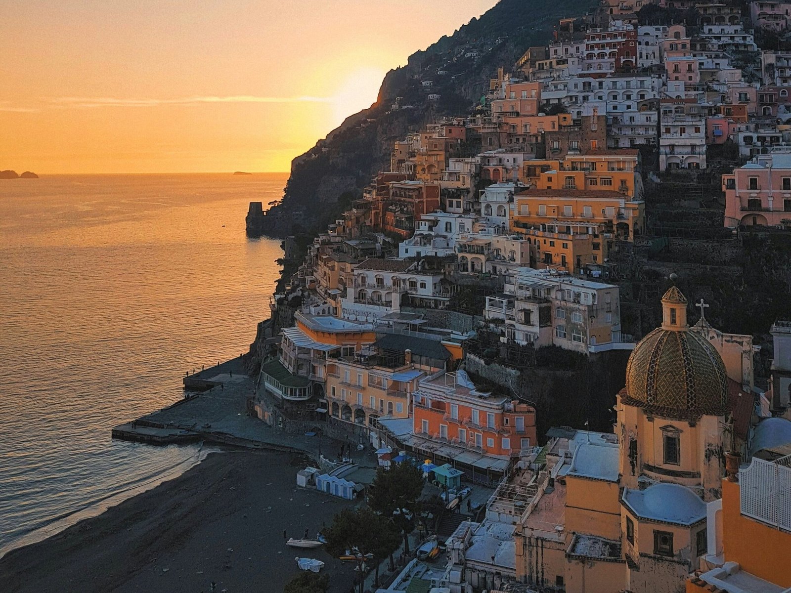Sunset view over Positano with colorful cliffside buildings, beach, and sea on Italy’s Amalfi Coast.