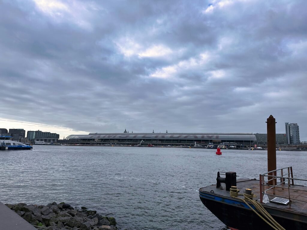 Amsterdam Centraal Station waterfront near busy canal cruise docks under cloudy sky
