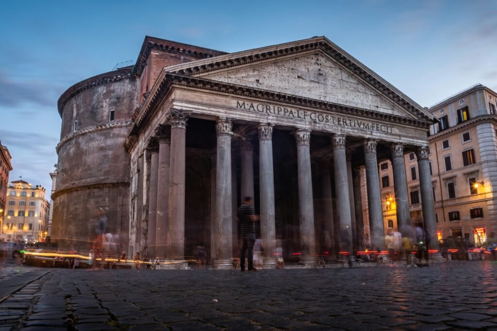 The Pantheon in Rome at dusk with columns, cobblestones, and people in the piazza