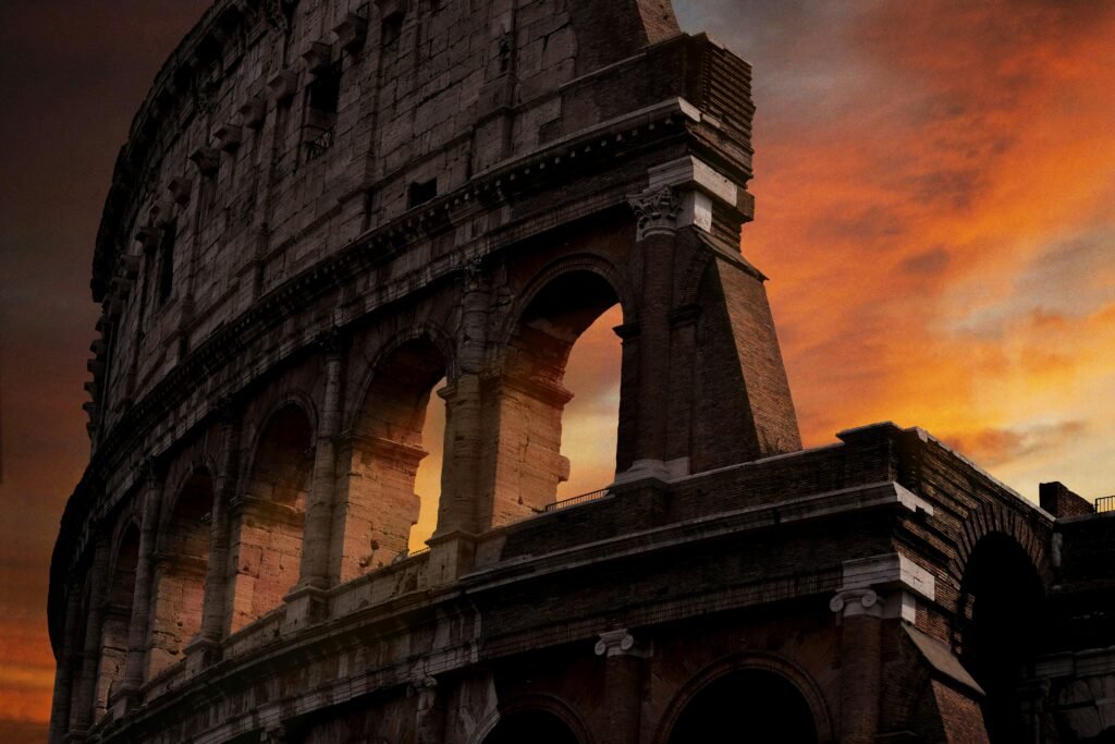 The Colosseum in Rome at sunset with orange clouds behind the ancient arches