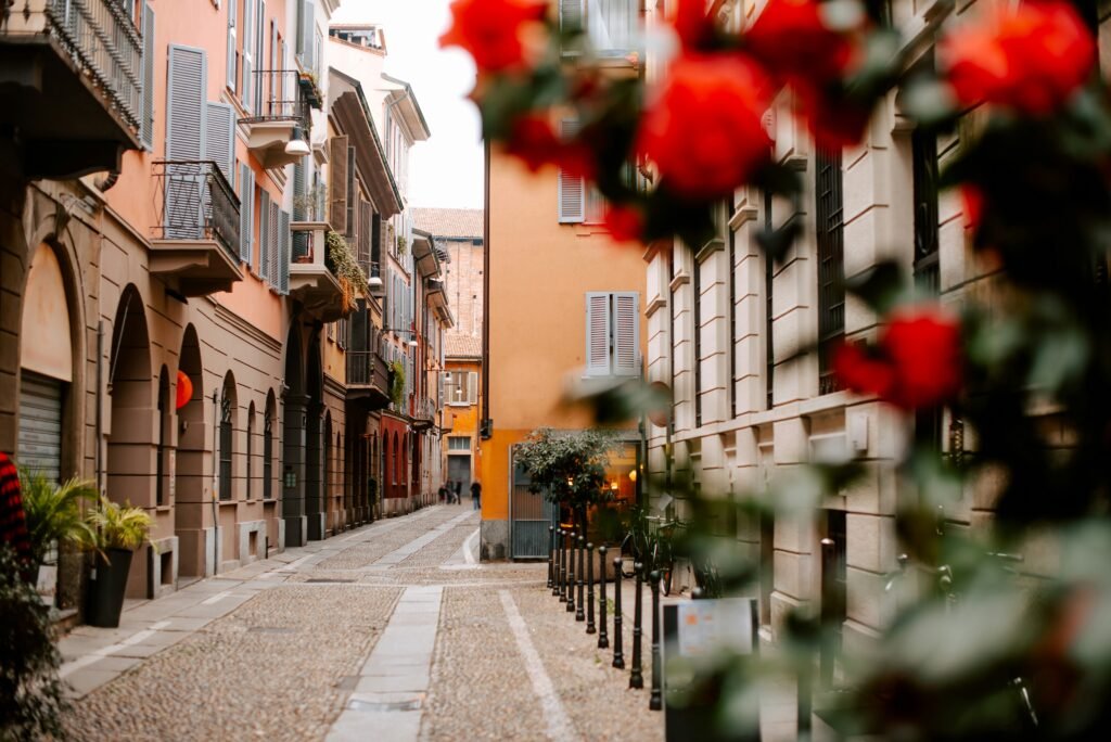 A quiet Monti street in Rome with pastel buildings, shutters, cobblestones, and red flowers