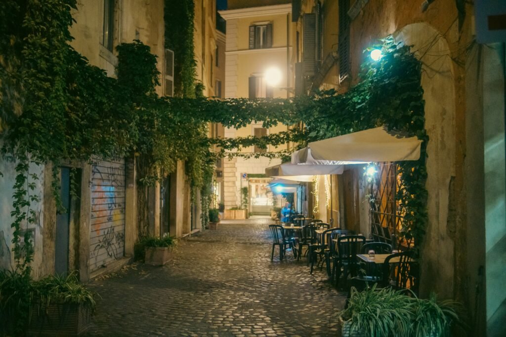 A quiet cobbled Trastevere street at night with ivy, warm lights, and outdoor restaurant tables