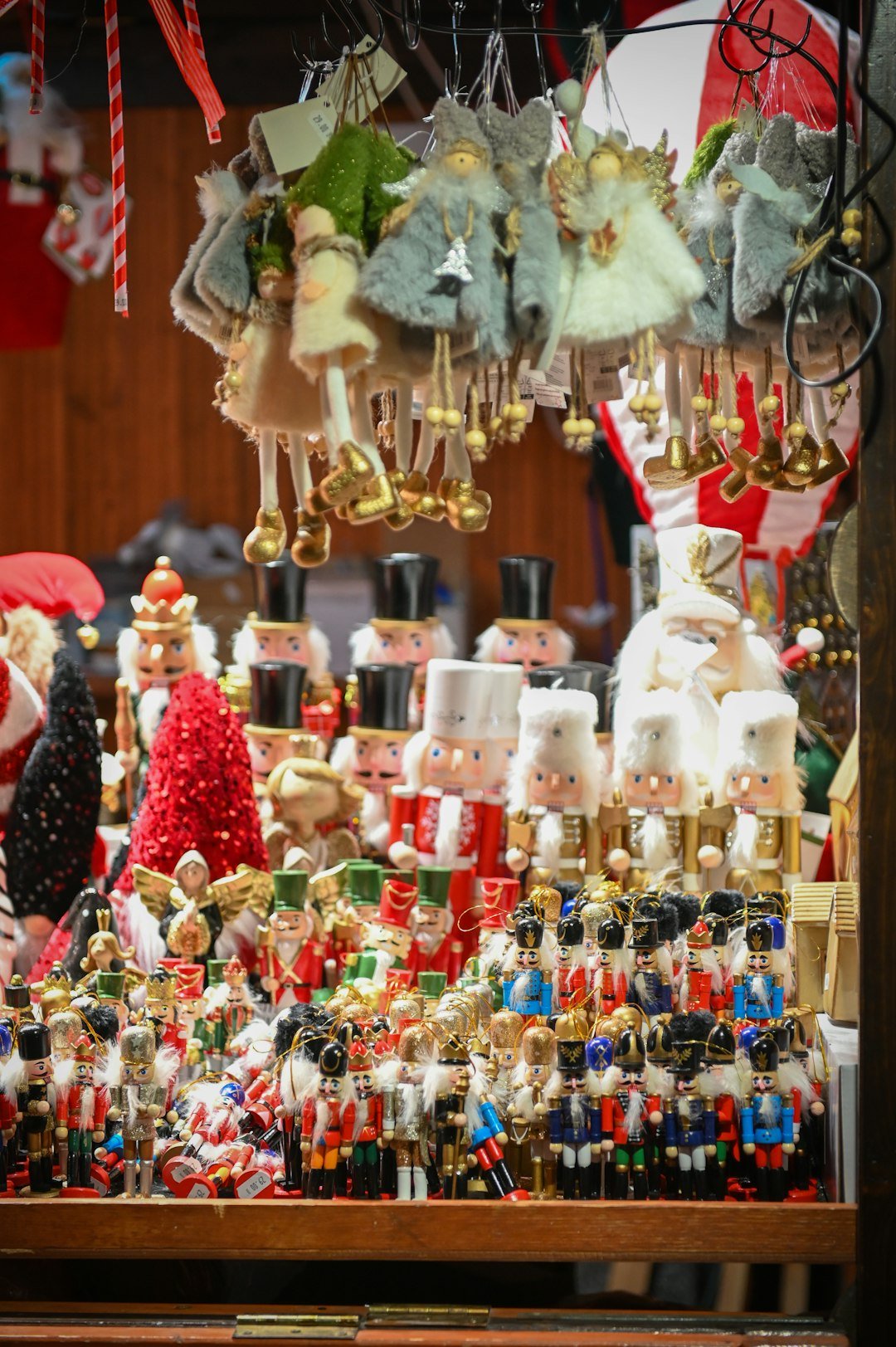 Rows of colorful hand-painted wooden nutcrackers in red, gold, and blue on display at a Christmas market stall, with angel ornaments hanging above