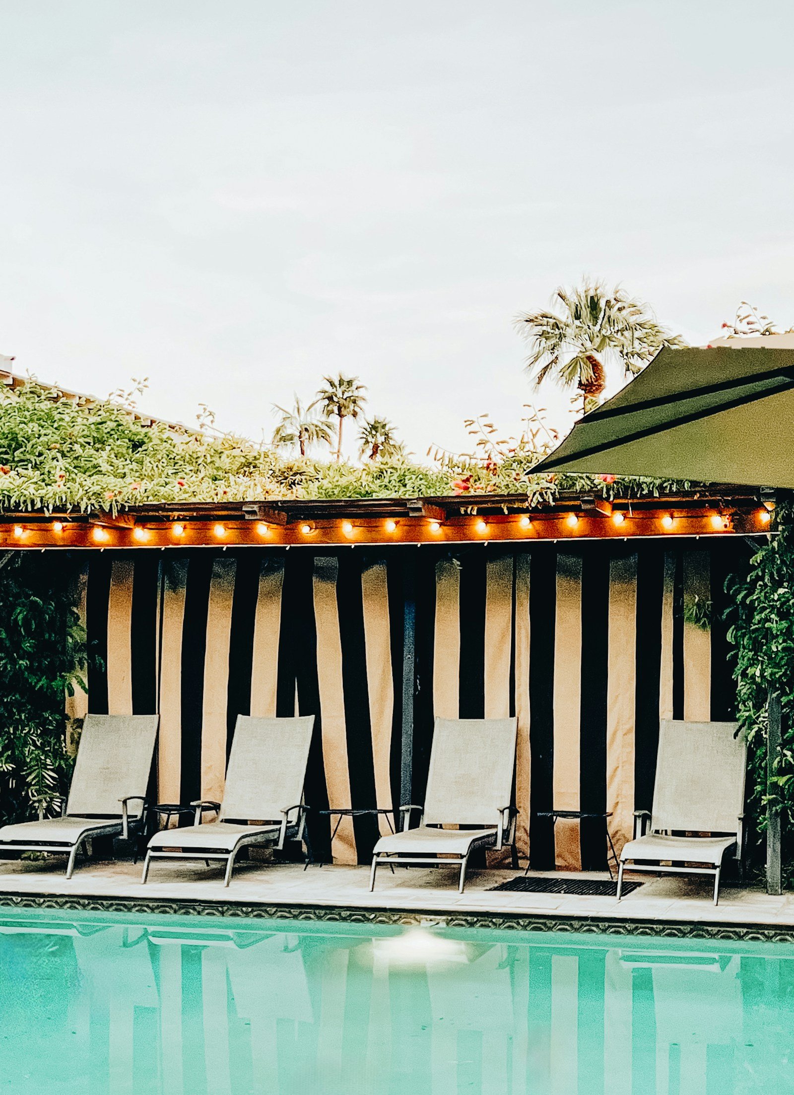 Pool loungers beside striped cabanas and palm trees at a Palm Springs resort