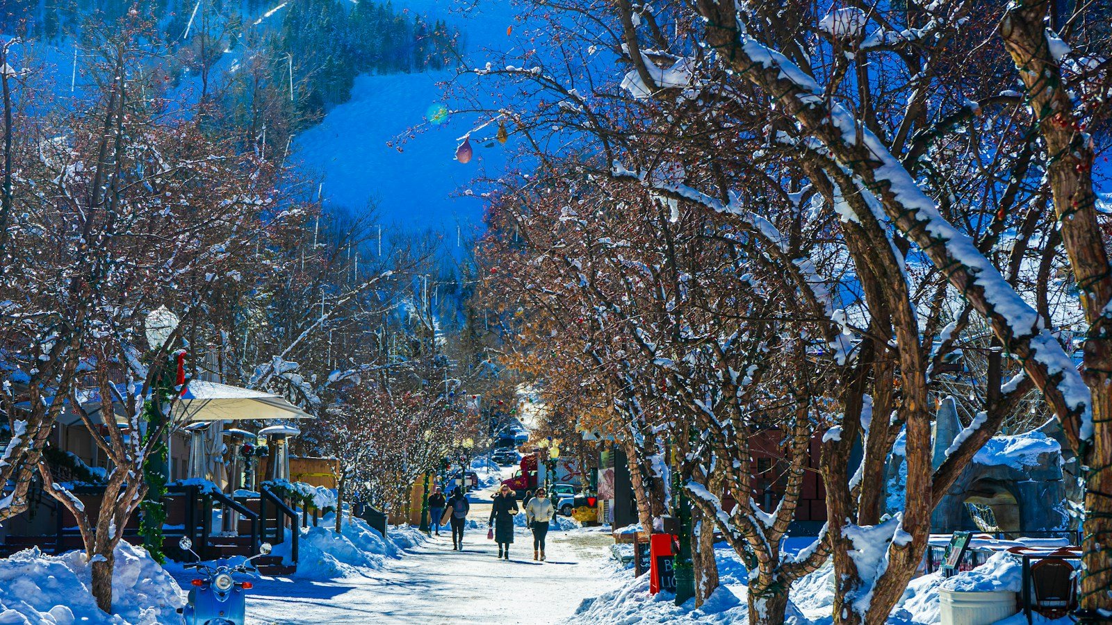 A snowy street in an American mountain resort town, framed by frosted trees with ski slopes visible behind