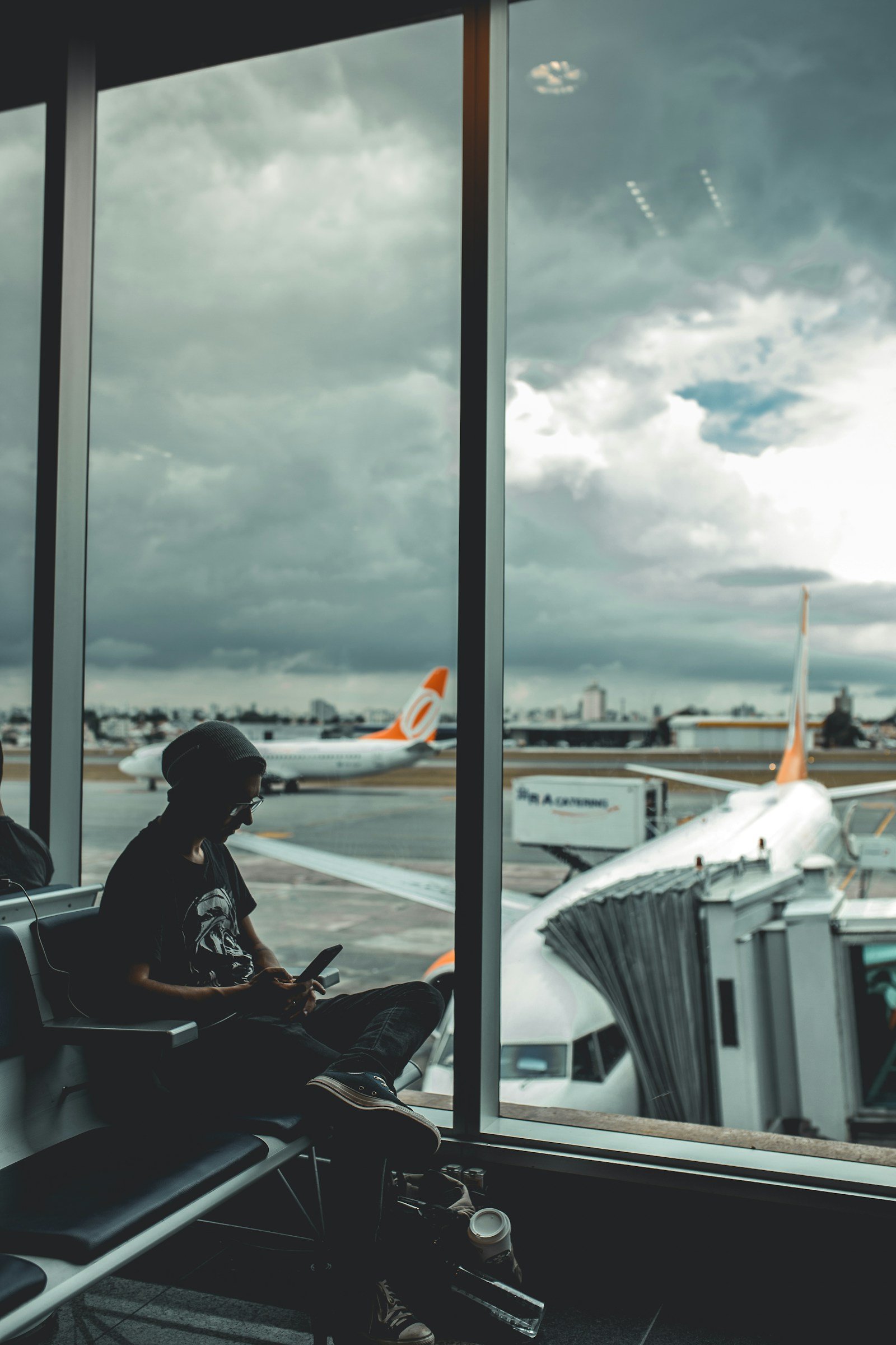 Traveler checking his phone at an airport gate window with planes visible outside