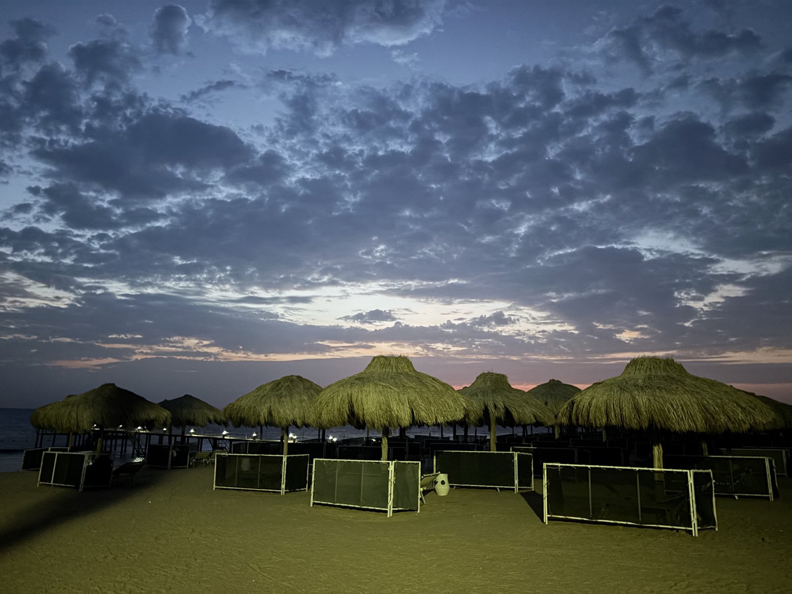 Straw-roofed beach umbrellas and sun loungers on a sandy beach under a dramatic dawn sky