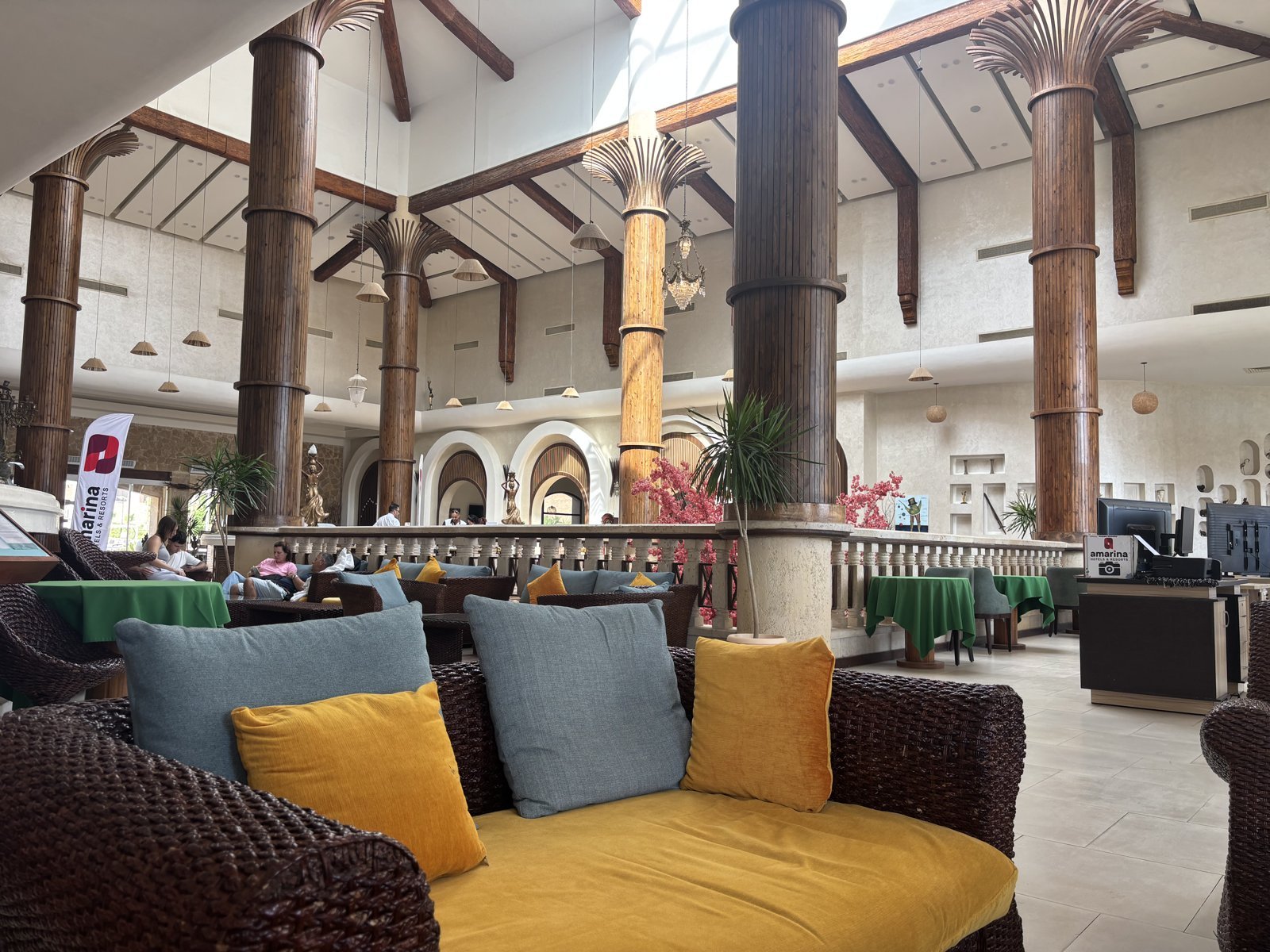 A hotel lobby lounge with wicker sofas, yellow and gray cushions and tall wooden columns