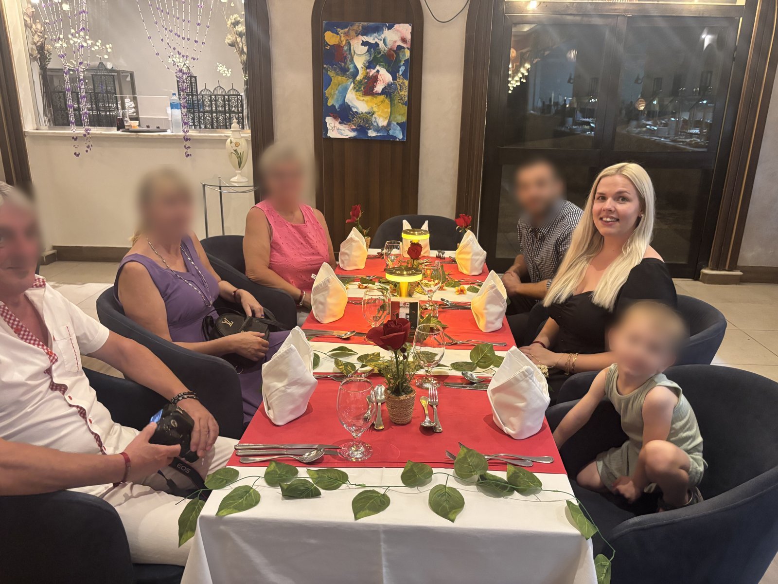 A long restaurant table set with red runners, roses and white napkins, with a family seated around it
