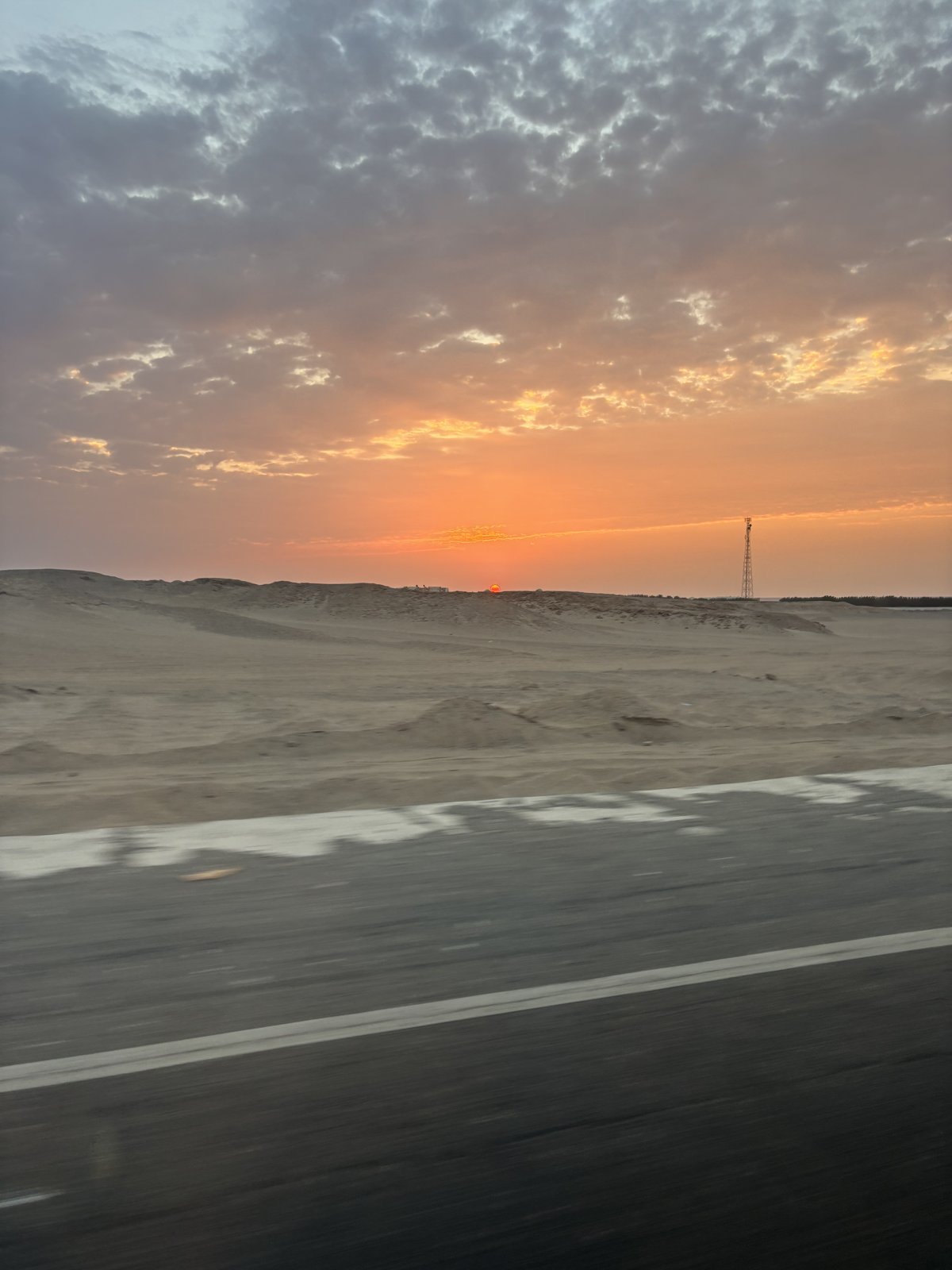 Sunrise over sand dunes beside an empty desert road in Egypt, seen from a moving car